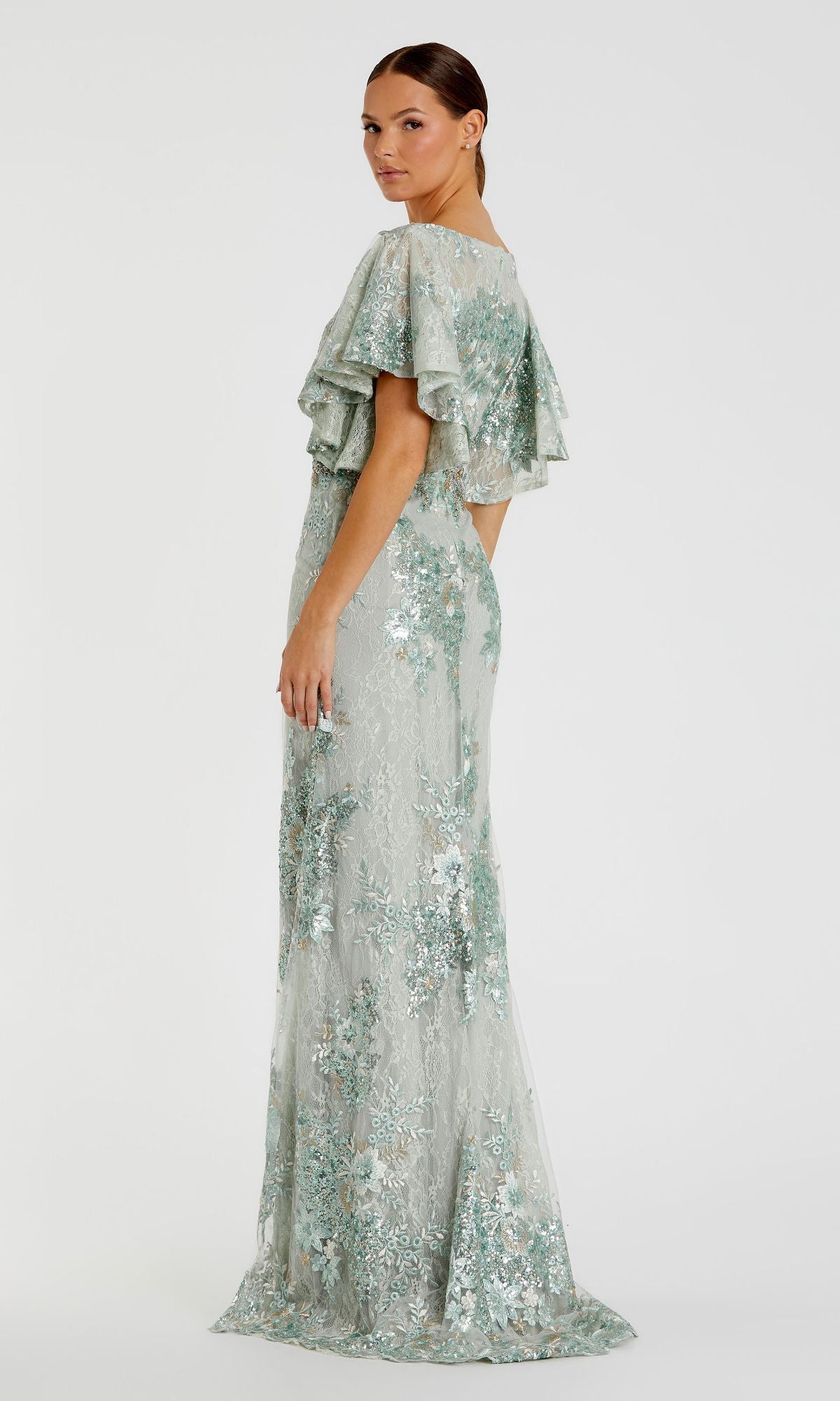 A woman poses in the Mac Duggal 67842 Flutter-Sleeve Long Formal Dress, featuring light green floral lace and ruffled short sleeves, shown from the side against a plain white background.